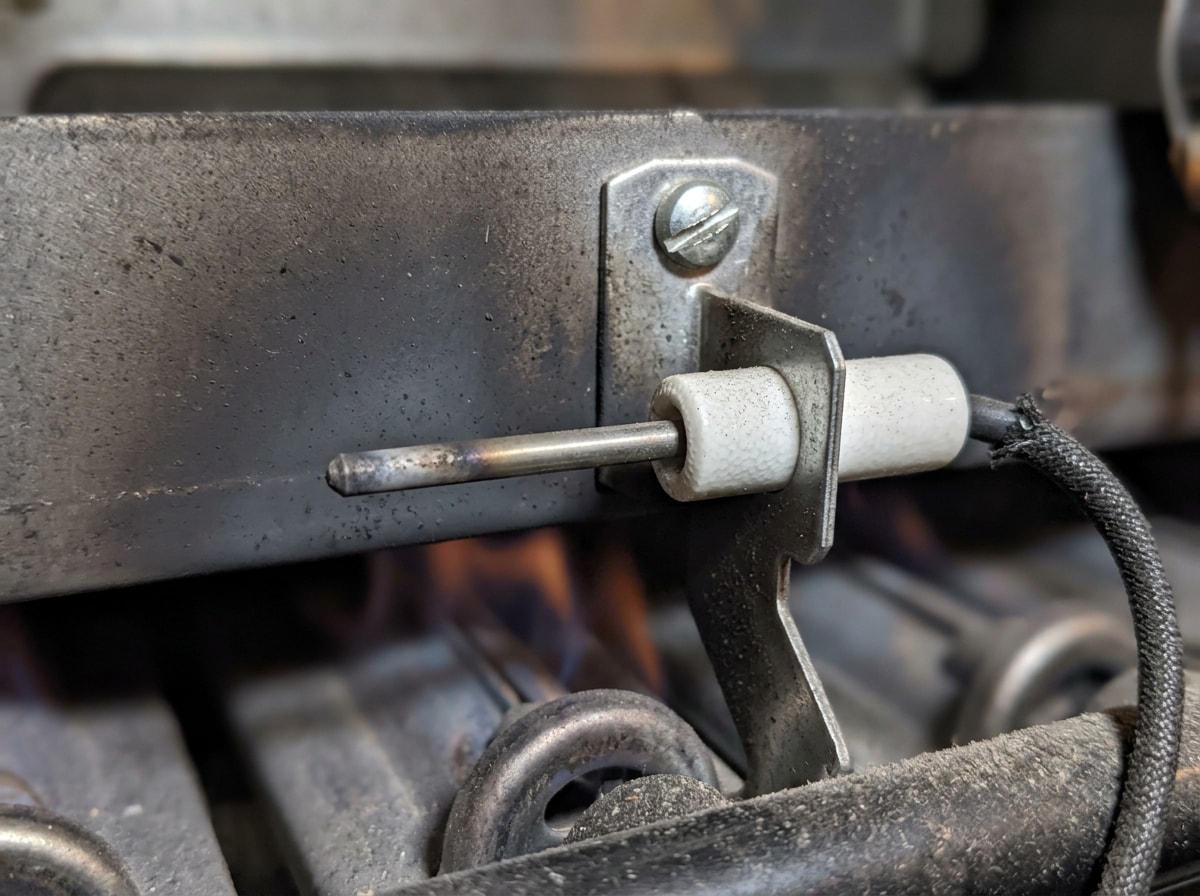 Close-up photo of a furnace flame sensor rod mounted near the burner assembly